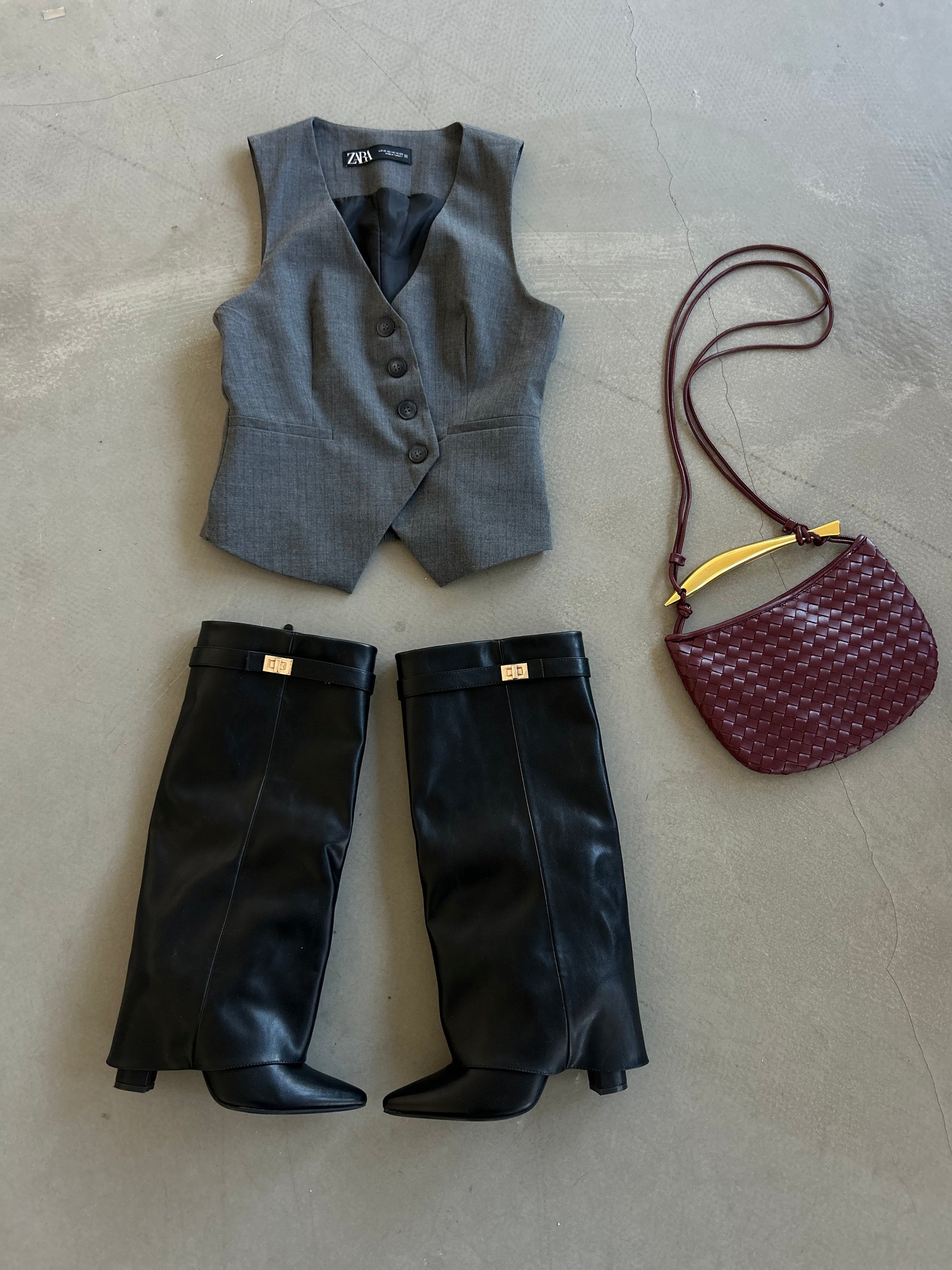 outfir inspiration for spring 2025 consisting of a woven burgundy purse with gold bar detail, black leather boots and grey waistcoat