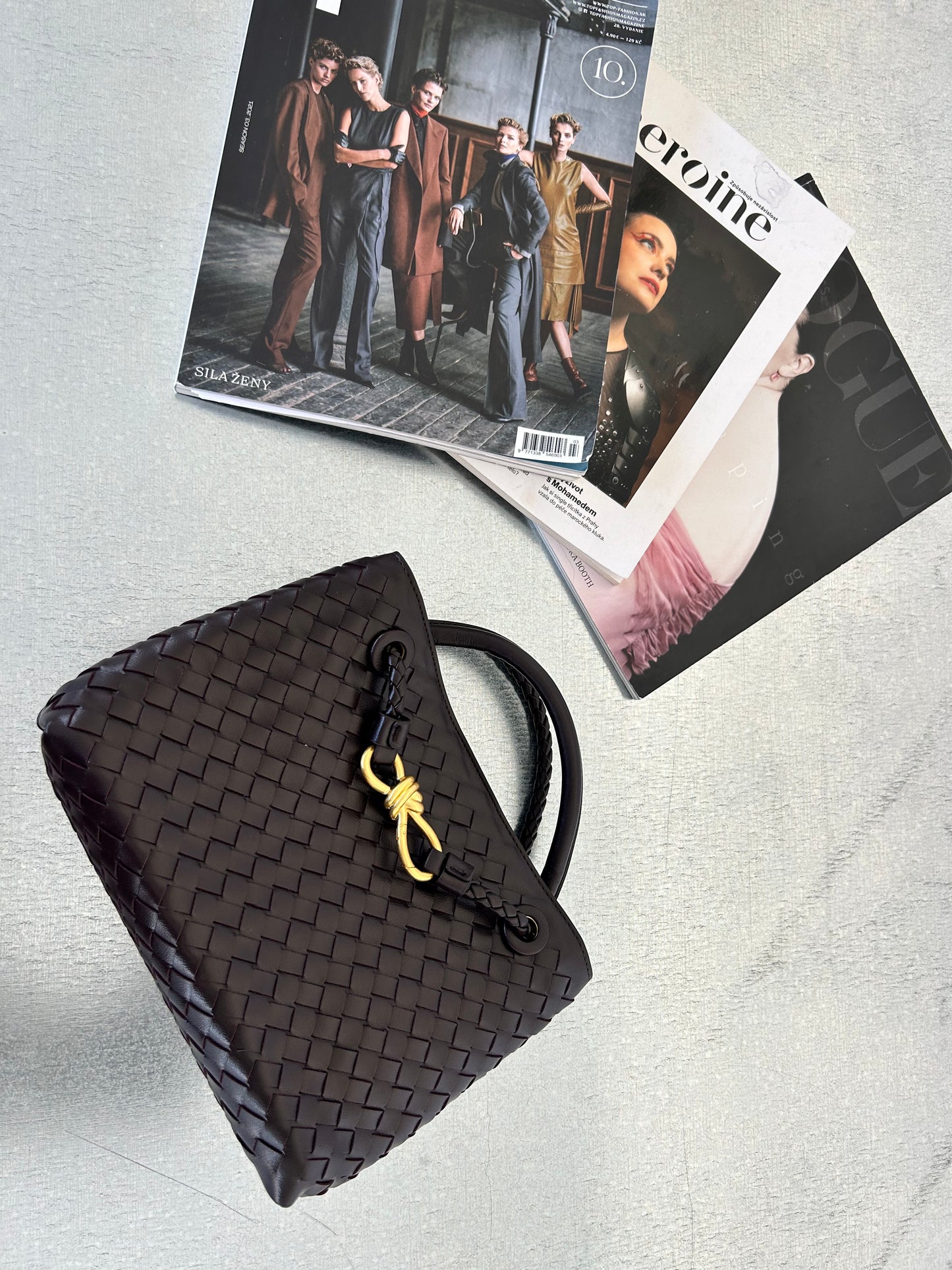 luxury box bag in coffee brown colour with crossbody adjustable strap.  Designer inspired woven shoulder bag placed on a metal table with aesthetically placed magazines.Interwoven handbag for women who love luxury and elegance. Knoten tasche for her
